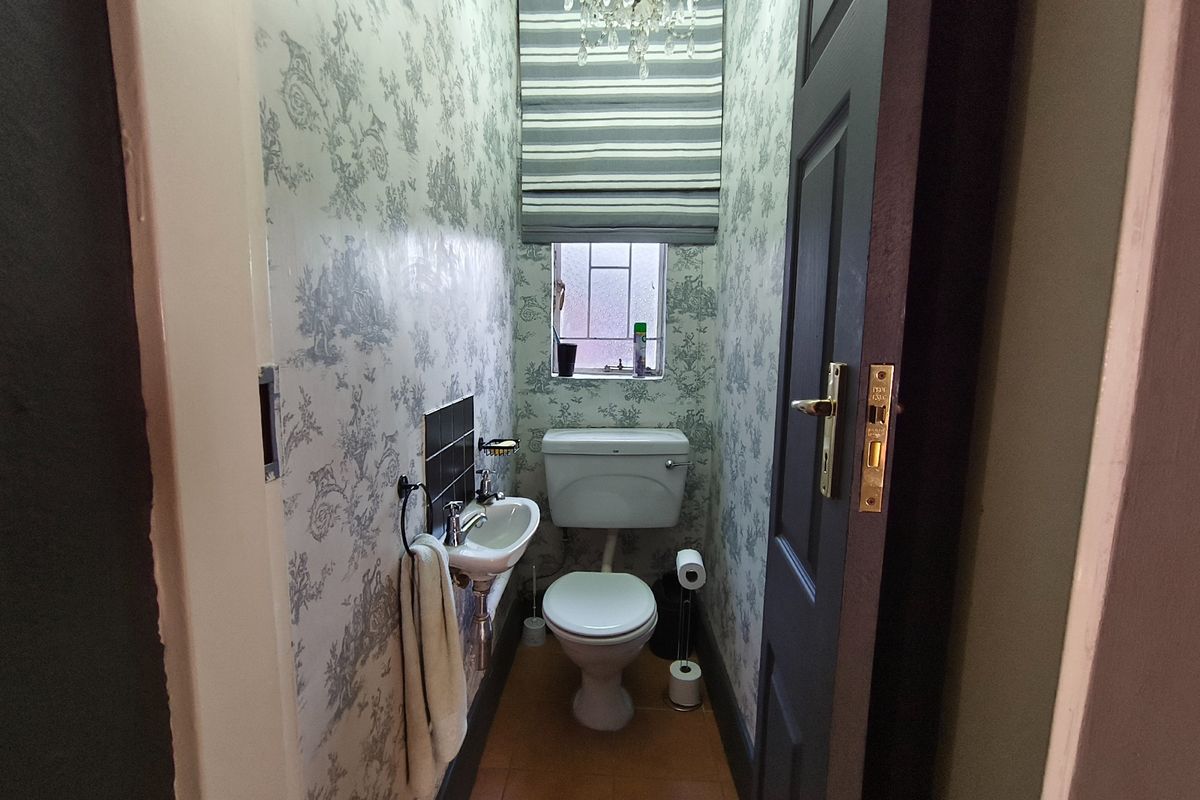 A compact guest powder room featuring a wall-mounted basin, toilet, and patterned wallpaper, providing a functional and private space.