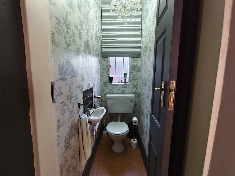 A compact guest powder room featuring a wall-mounted basin, toilet, and patterned wallpaper, providing a functional and private space.