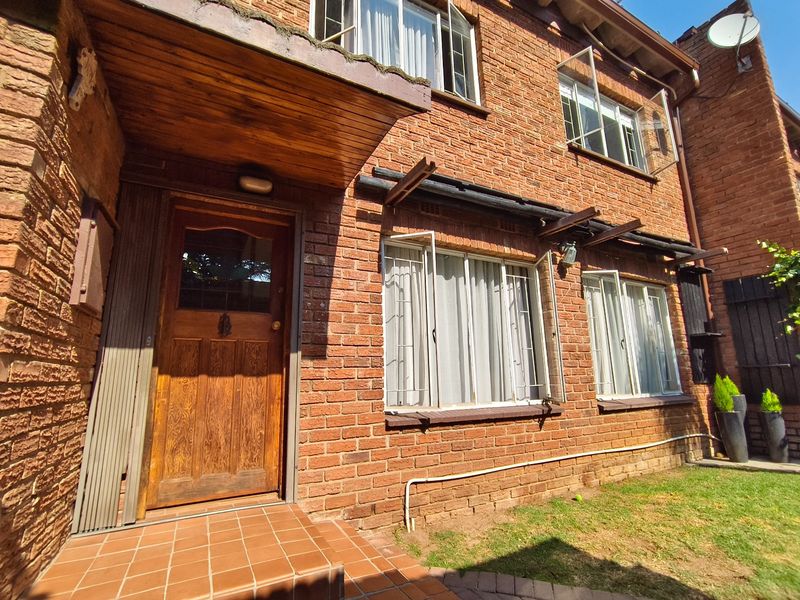 Front facade of a classic brick townhouse featuring a covered entrance, timber front door, and metal-framed windows with security bars.