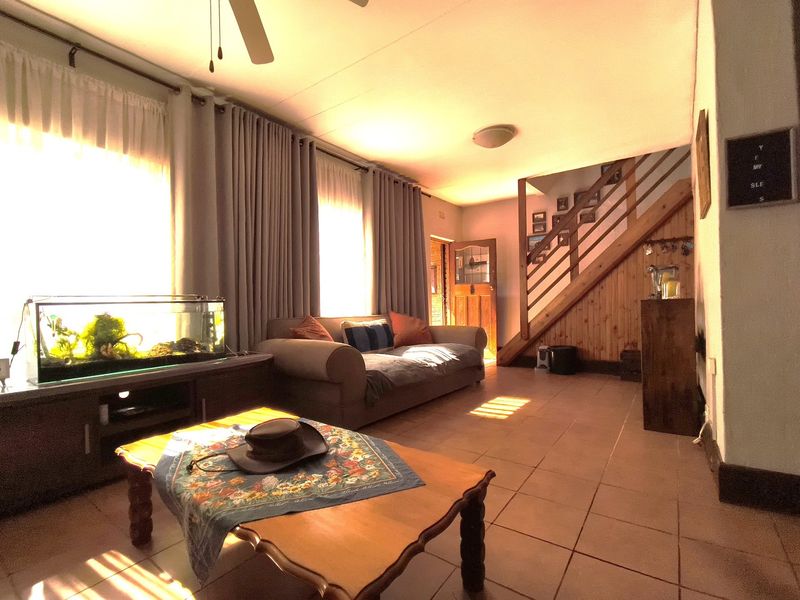 Spacious living area featuring tiled flooring, a wooden staircase with integrated railing, and large windows allowing for ample natural light.