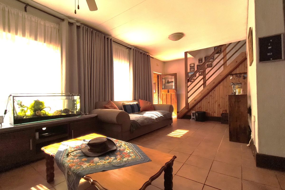 Spacious living area featuring tiled flooring, a wooden staircase with integrated railing, and large windows allowing for ample natural light.