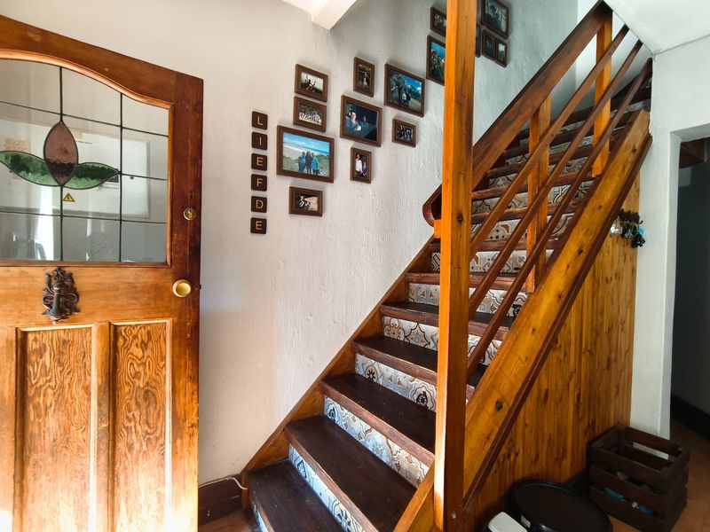 An interior entryway featuring a wooden staircase with decorative tiled risers and a solid timber front door with leaded glass detailing.