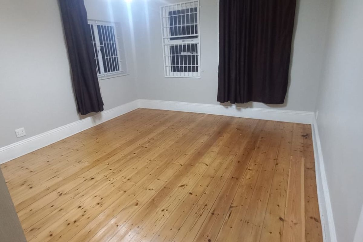 A spacious bedroom featuring polished timber flooring, neutral wall finishes, and security bars on the windows.