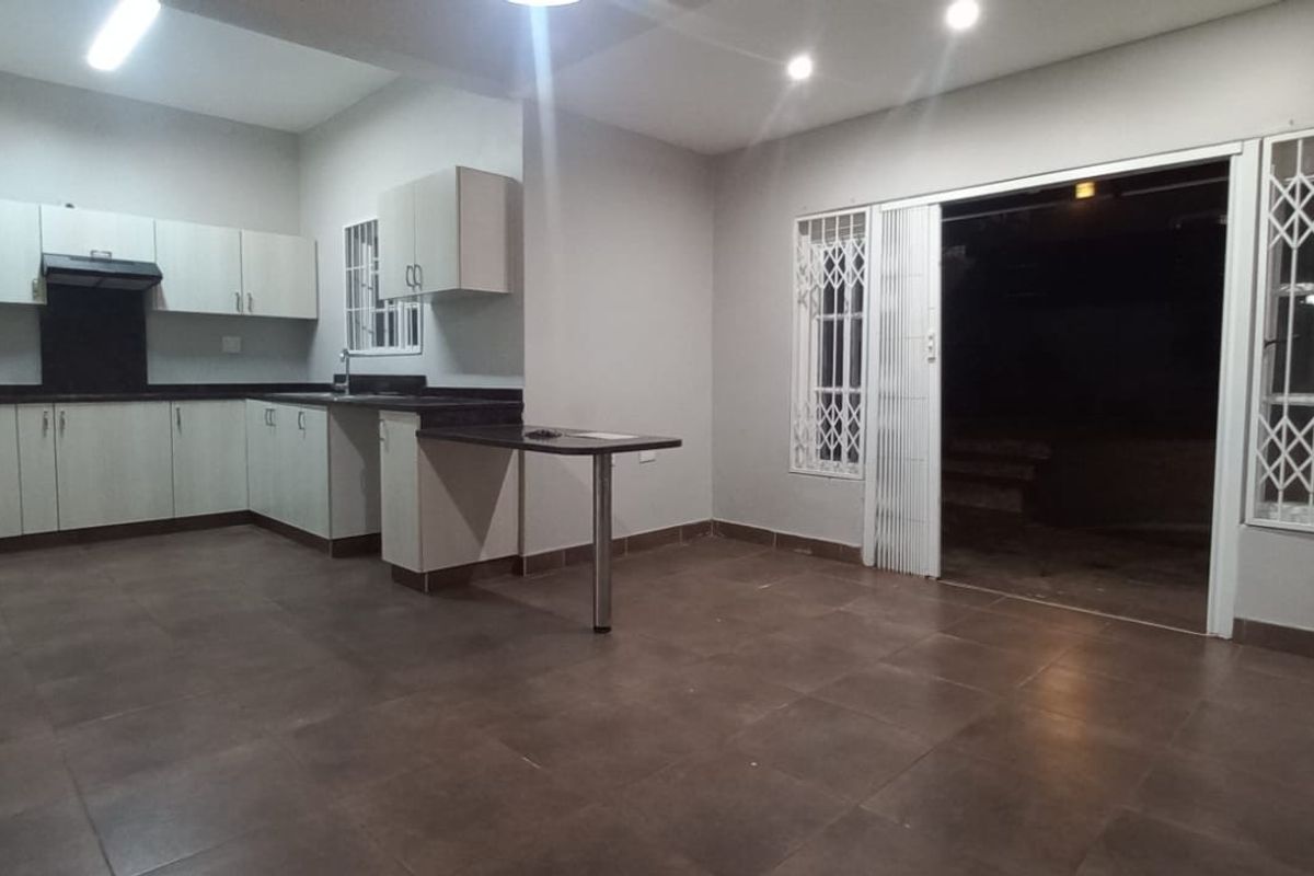 Open plan kitchen and living area featuring tiled flooring, built-in cabinetry, and sliding doors with security gates leading to the exterior.