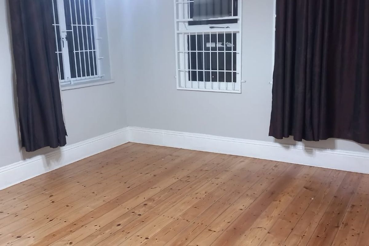 A bright, empty bedroom featuring polished timber flooring, neutral wall tones, and security bars fitted to the windows.