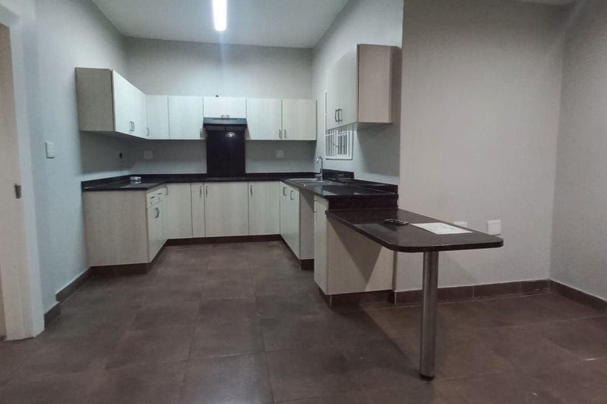 A functional kitchen featuring light-toned cabinetry, dark countertops, a breakfast bar, and tiled flooring, with security bars on the windows.
