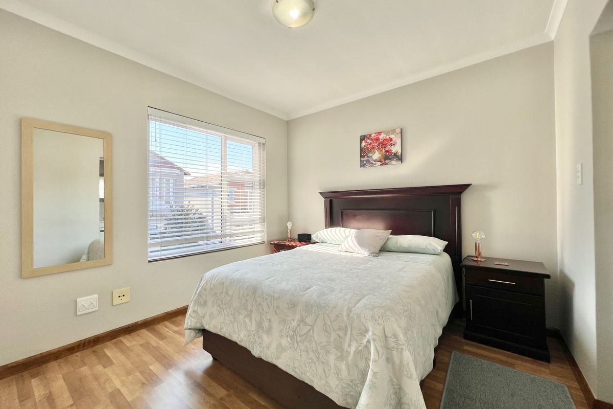 A well-maintained bedroom featuring laminate wood flooring, neutral wall tones, and a large window with fitted blinds, providing ample natural light.