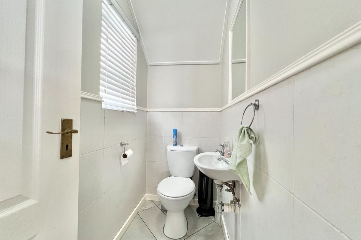 A compact guest bathroom featuring a white toilet, wall-mounted basin, tiled walls, and a window with fitted blinds.