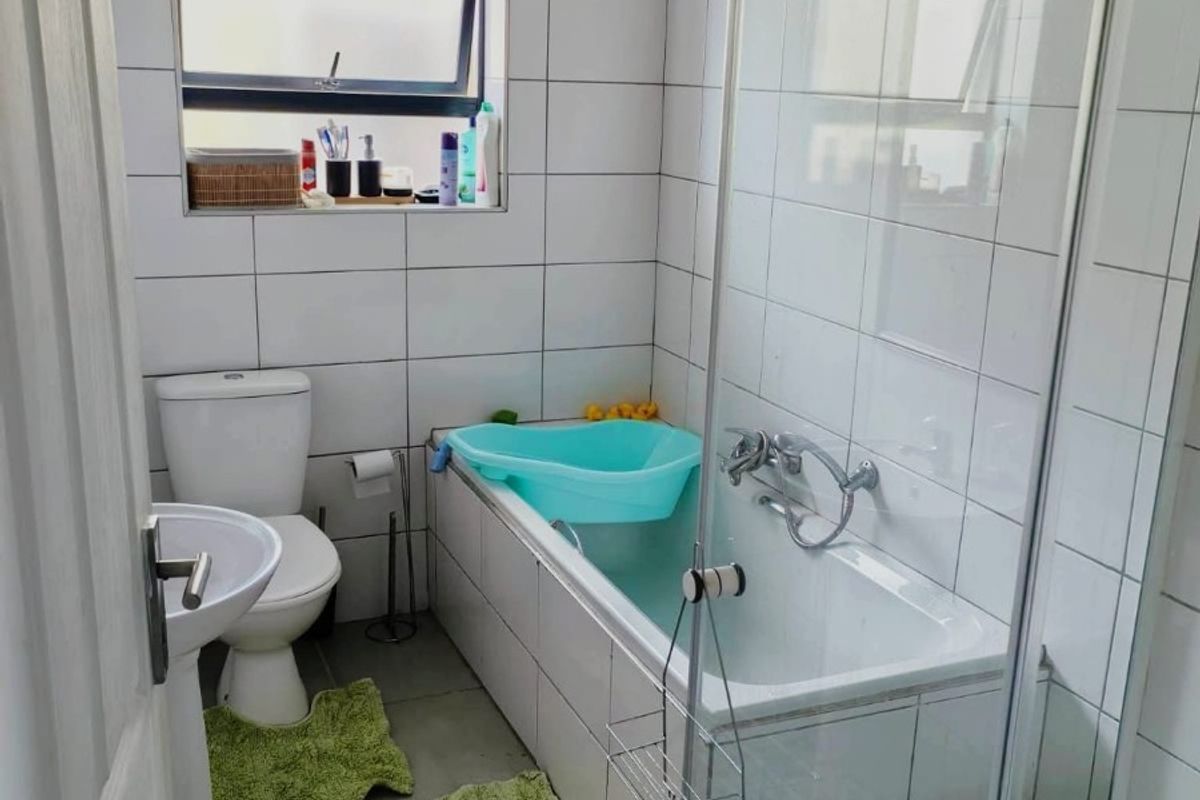 A compact bathroom featuring a white pedestal basin, toilet, and a combined shower and bathtub unit with glass enclosure.