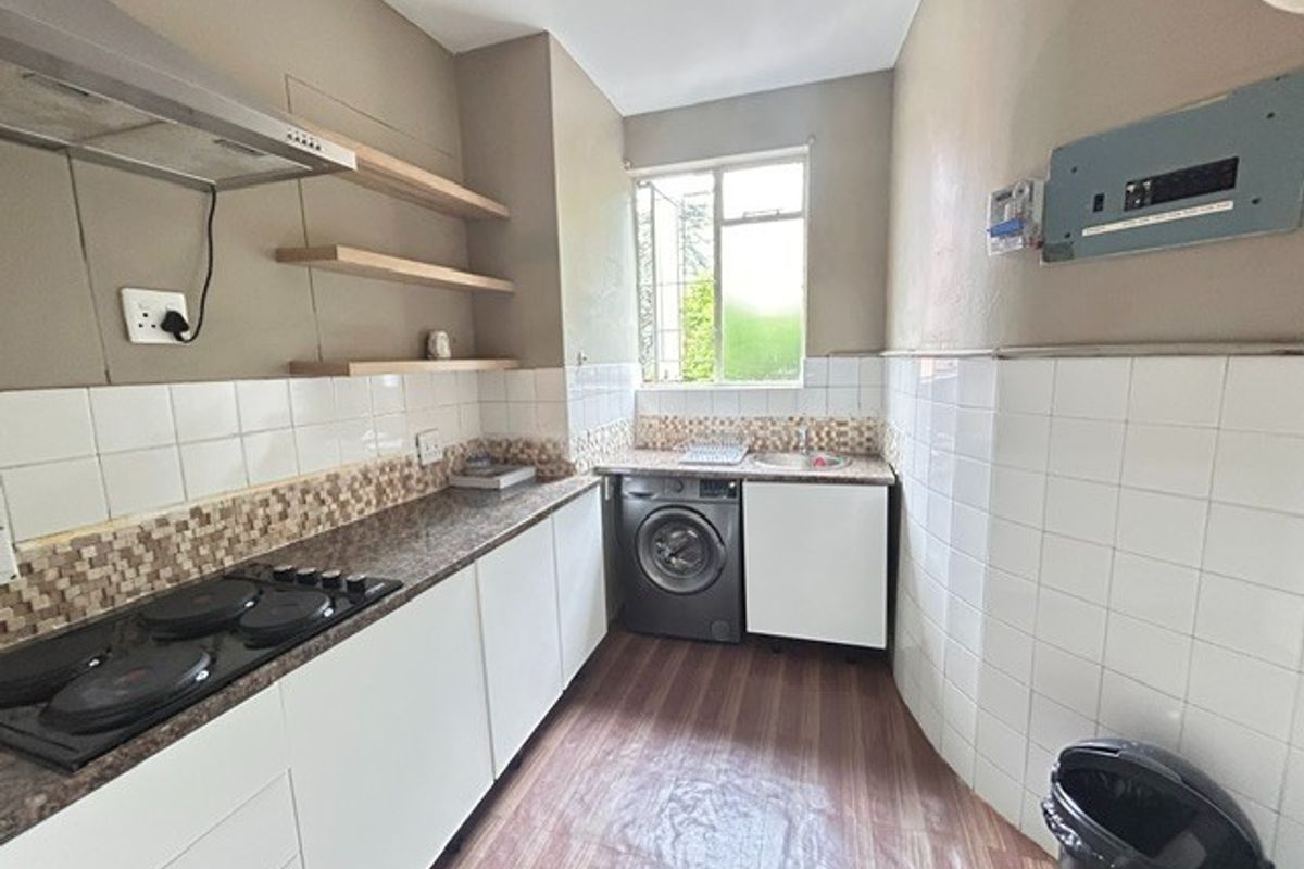 Compact kitchen featuring white cabinetry, granite countertops, built-in electric hob, extractor fan, and integrated laundry space with tiled splashbacks.