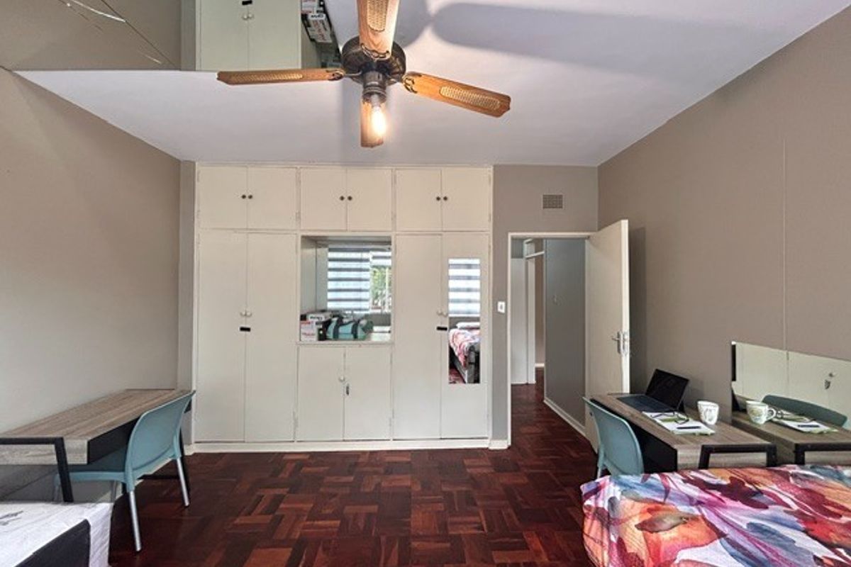 Bedroom featuring parquet flooring, built-in cupboards with integrated mirror, and a ceiling fan.