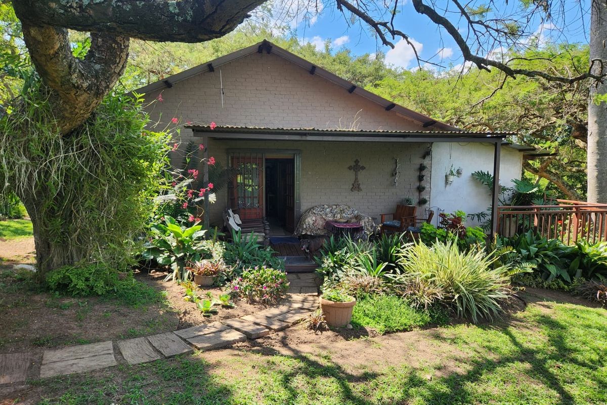 A rear view of a small holding dwelling featuring a covered patio, brick facade, and established garden surroundings.