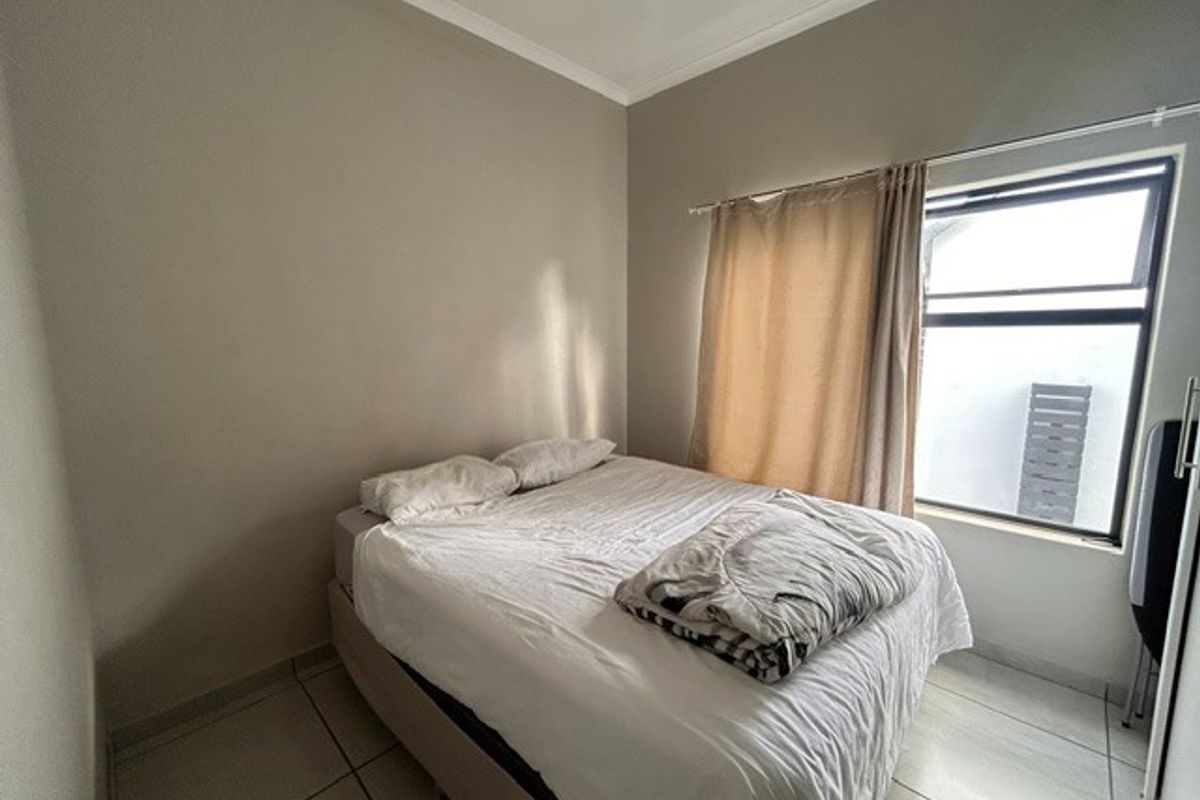 A functional bedroom featuring neutral wall tones, tiled flooring, and a window providing natural light.