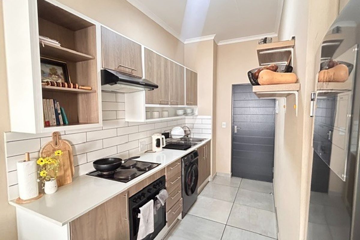 Modern galley-style kitchen featuring wood-grain cabinetry, white subway tile backsplash, integrated oven, hob, extractor fan, and tiled flooring.
