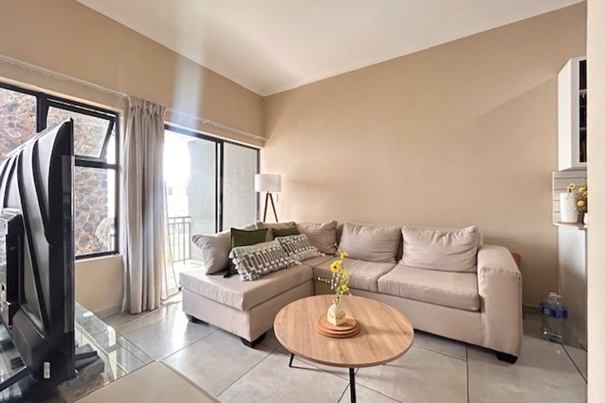 A bright living room featuring large sliding glass doors that open to a balcony, tiled flooring, and neutral wall tones.