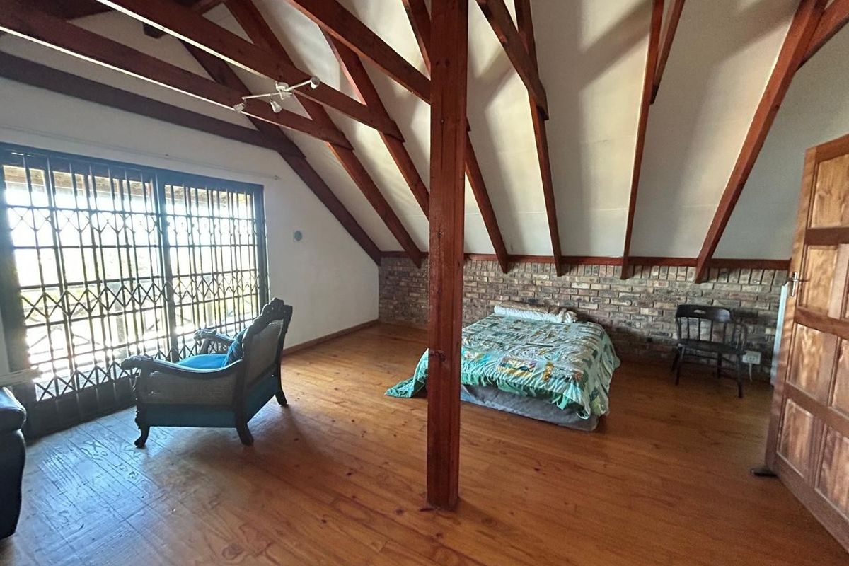 Spacious bedroom featuring exposed timber roof trusses, warm timber flooring, and an exposed brick feature wall with access to a balcony via security gate.