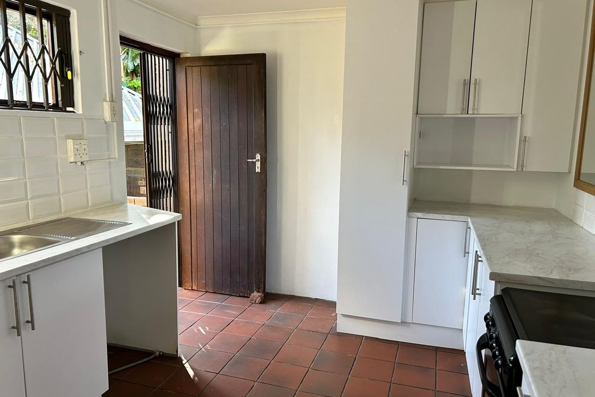 A functional kitchen featuring white cabinetry, laminate countertops, tiled flooring, and direct access to the exterior through a secure door.