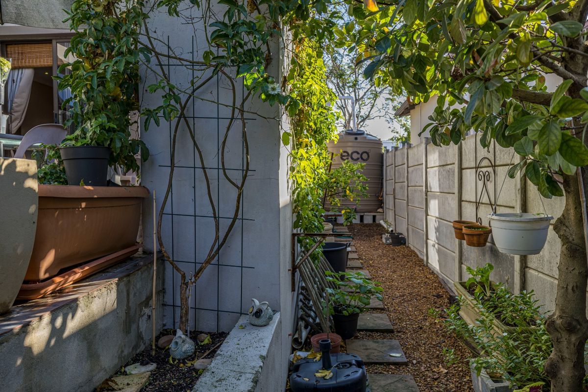 A narrow side garden area featuring a gravel pathway, precast concrete boundary wall, and a water storage tank.
