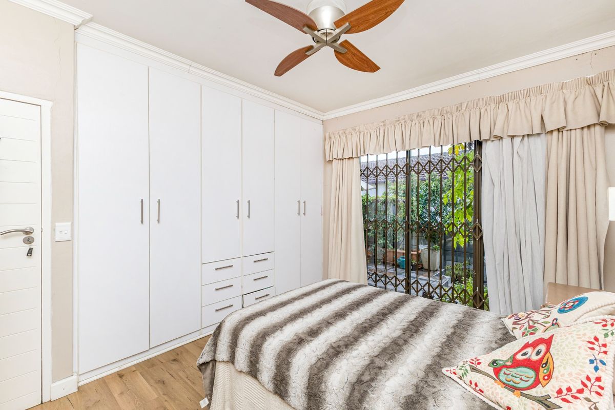 A bedroom featuring extensive white built-in cupboards, a ceiling fan, and a sliding door with a security gate leading to the exterior.