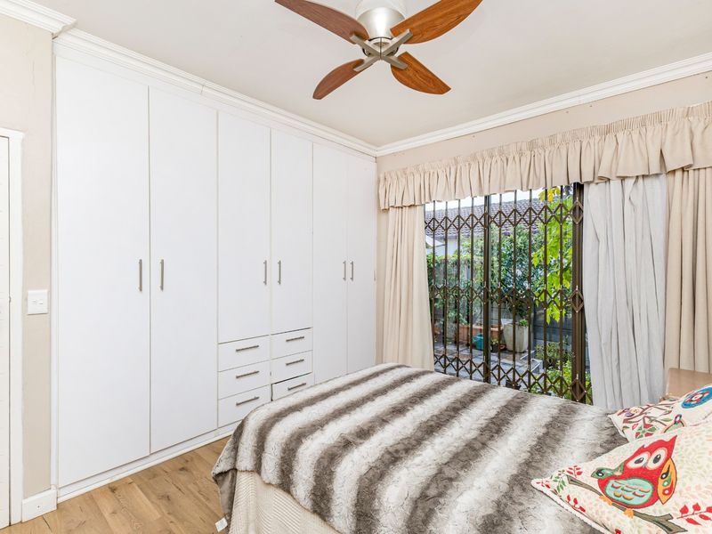 A bedroom featuring extensive white built-in cupboards, a ceiling fan, and a sliding door with a security gate leading to the exterior.