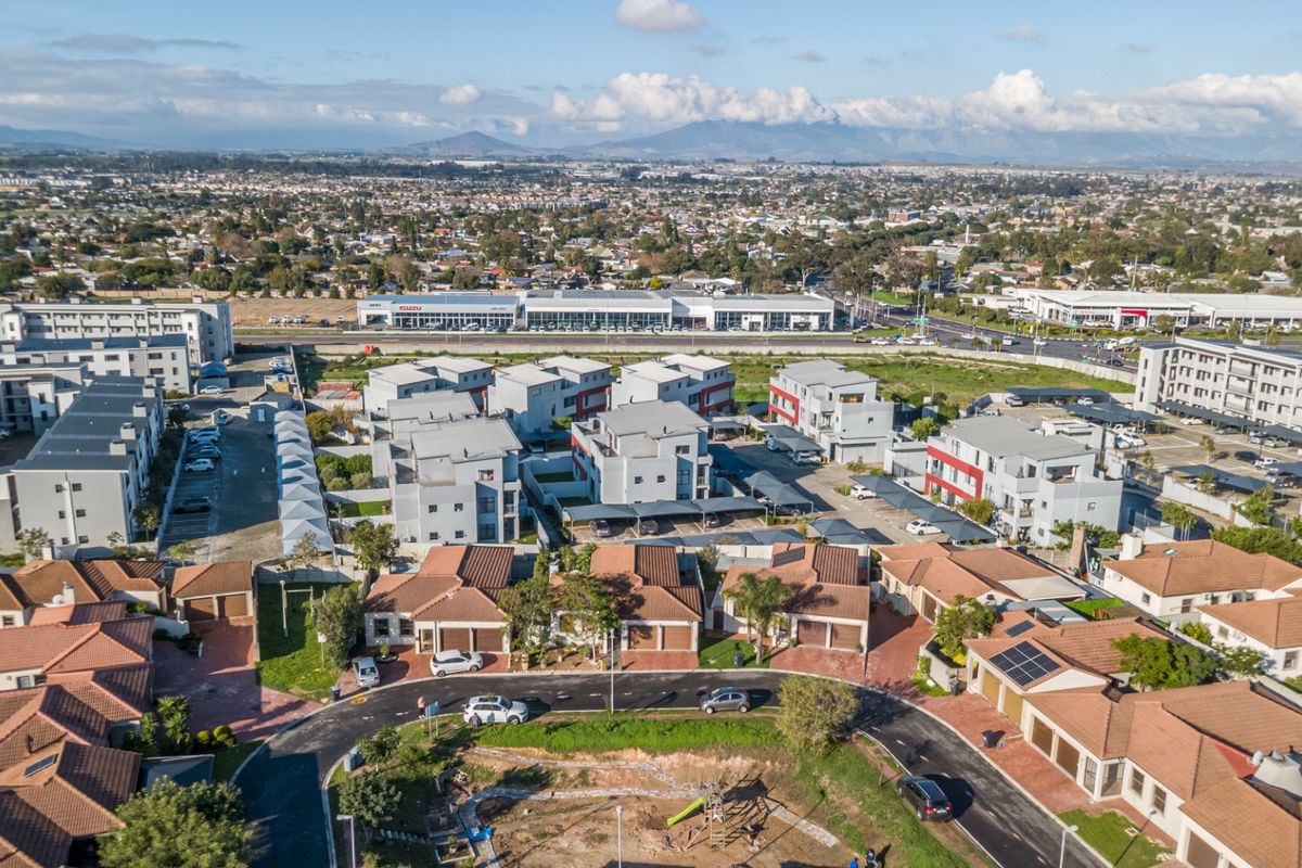 An aerial view of a residential estate featuring multiple houses with tiled roofs, paved driveways, and carports, set within a suburban landscape.