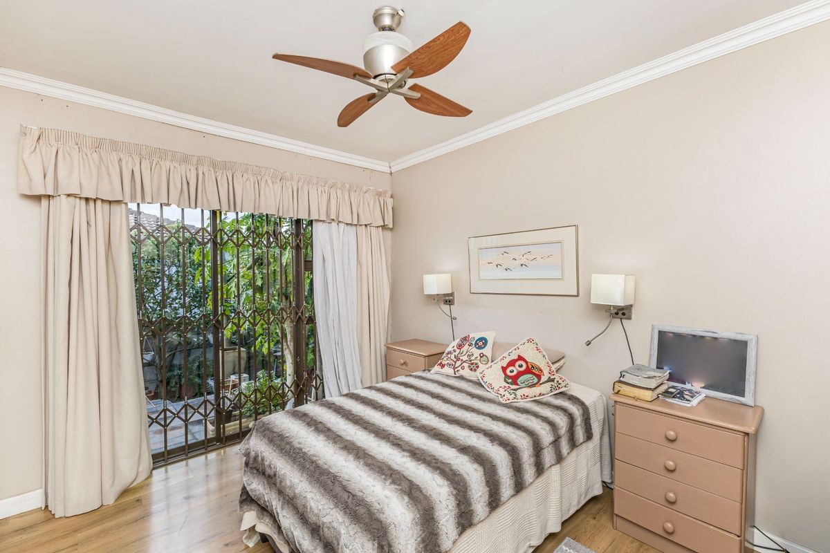 A bedroom featuring laminate flooring, a ceiling fan, and sliding glass doors with security gates leading to an outdoor area.
