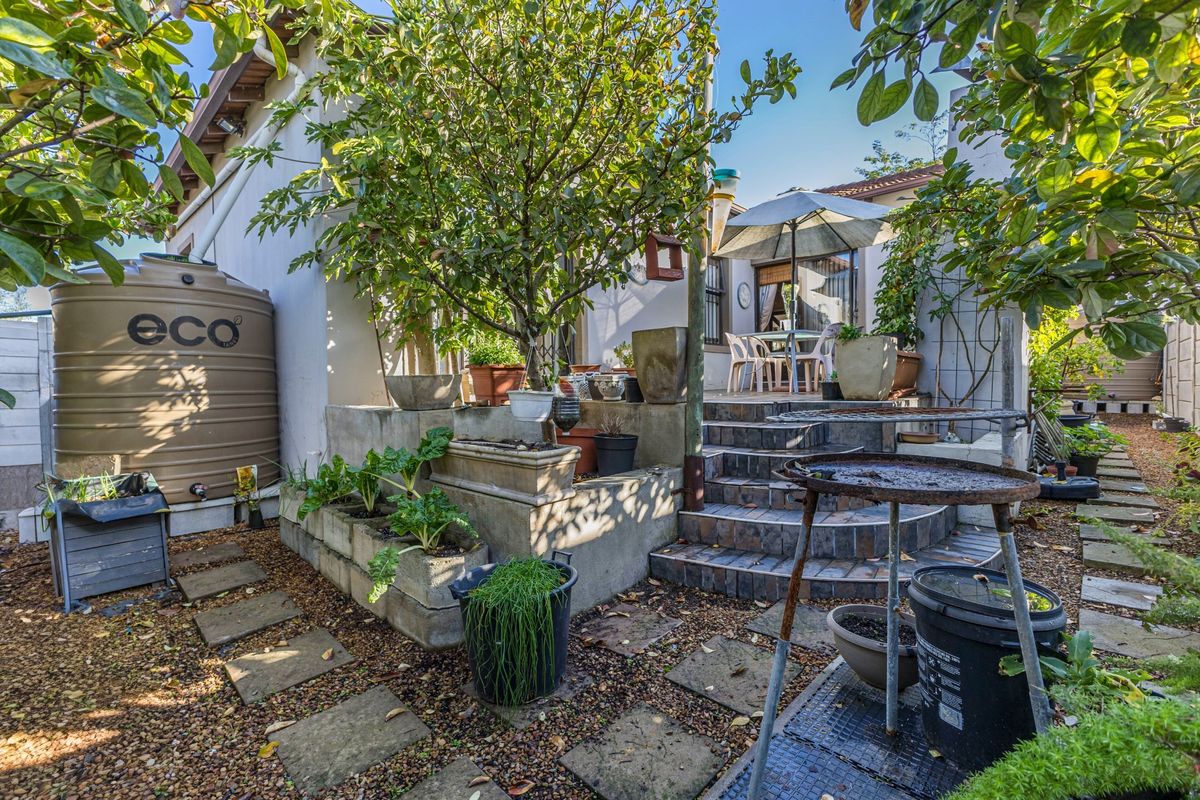 A rear garden area featuring a raised patio with tiled steps, a water storage tank, and established landscaping.