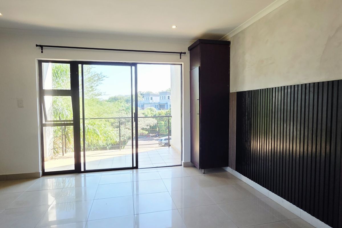 A bright bedroom featuring tiled flooring, built-in cabinetry with decorative slat paneling, and sliding glass doors opening onto a private balcony.