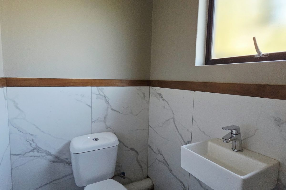 A compact guest bathroom featuring modern marble-look wall tiles, a wall-mounted basin, and a toilet with a wooden trim finish.