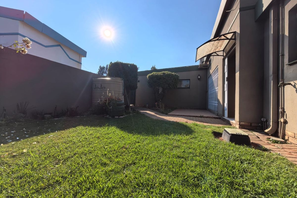 A private rear garden area featuring a lawn, paved walkway, and a water storage tank adjacent to the townhouse structure.