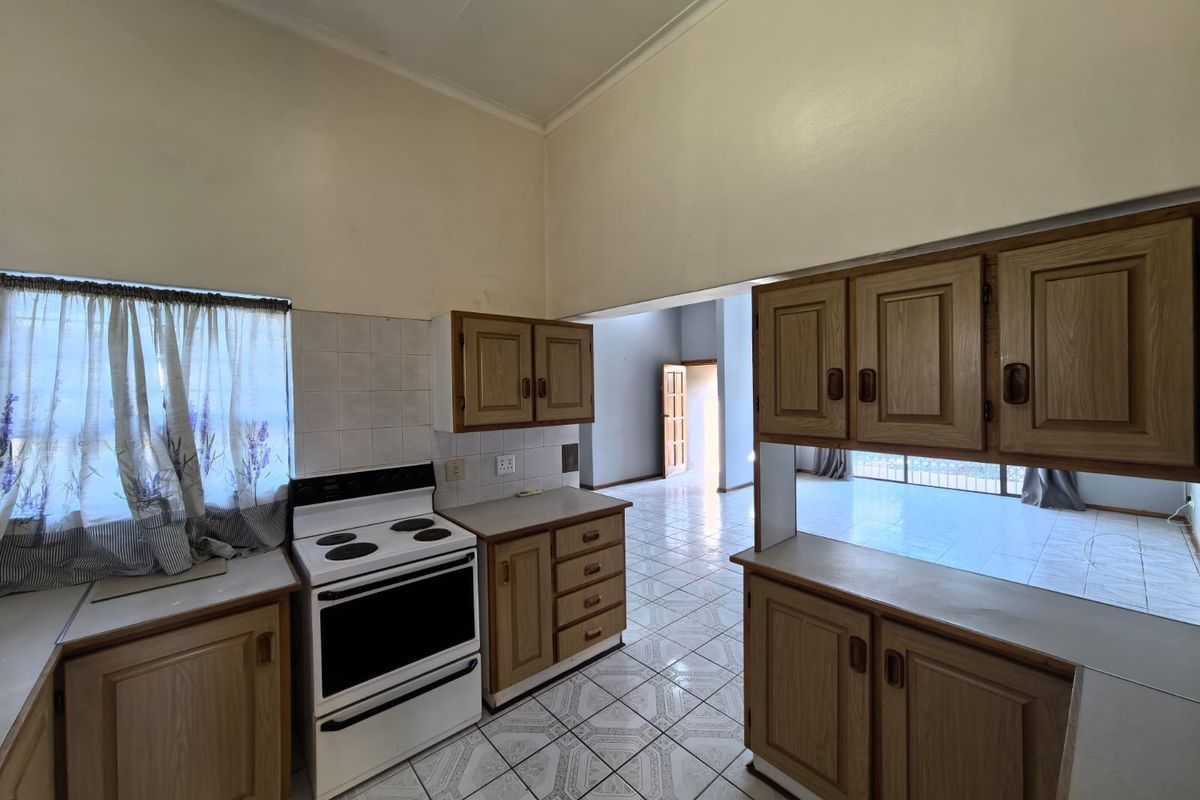 A dated kitchen featuring wood-finish cabinetry, tiled flooring, and a freestanding stove, opening into an adjacent living area.
