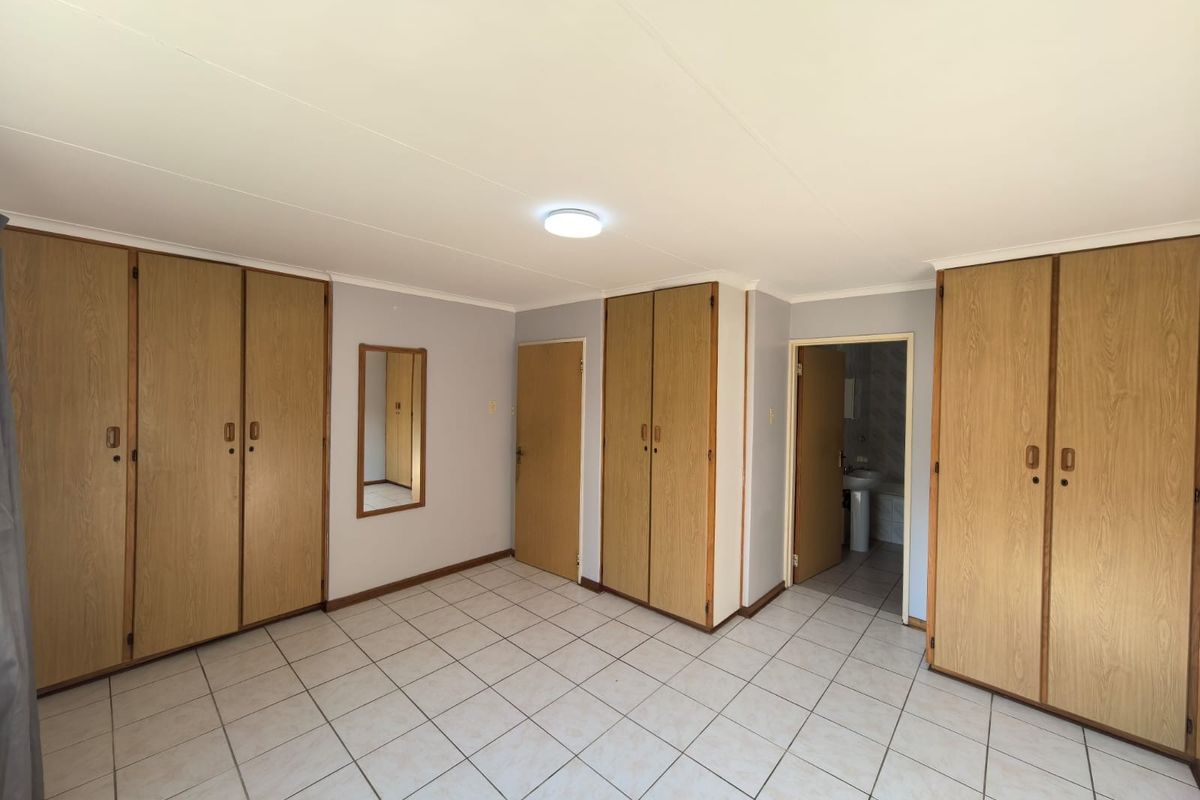 A spacious bedroom featuring extensive built-in wooden cabinetry, neutral wall finishes, and tiled flooring, with direct access to an adjoining bathroom.