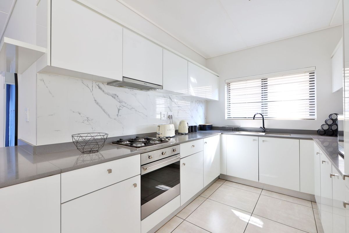 Modern kitchen featuring white high-gloss cabinetry, stone countertops, marble-look splashback, built-in oven, gas hob, and a sleek black faucet.