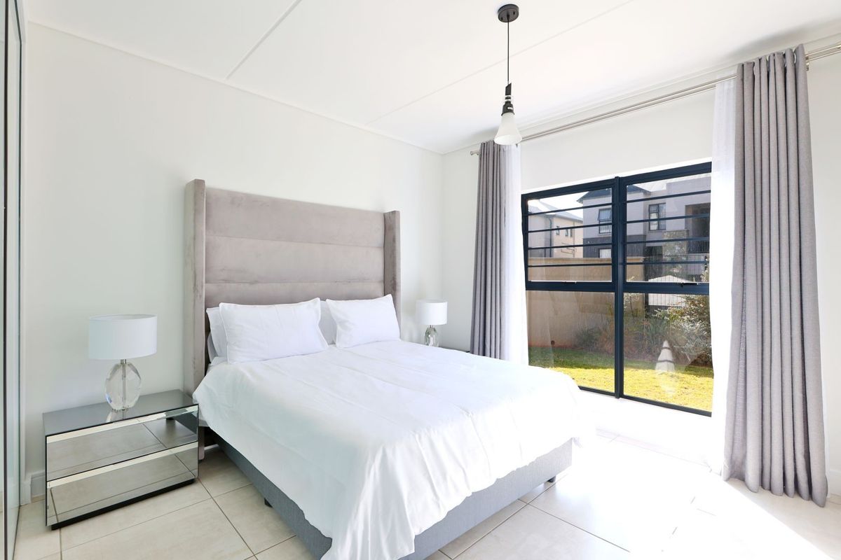 A bright and modern bedroom featuring large windows with security bars, tiled flooring, and a neutral color palette.