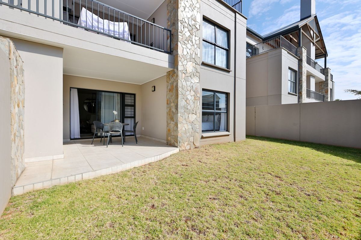 Ground floor apartment featuring a tiled patio area, stone-clad feature pillar, and a private garden space with modern exterior finishes.