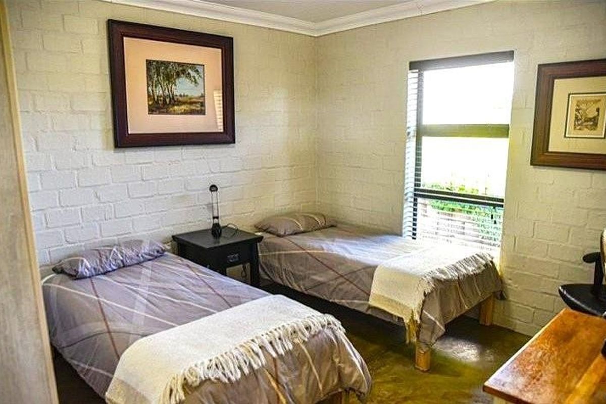 A bedroom featuring painted brick walls, a large window with blinds, and concrete flooring.