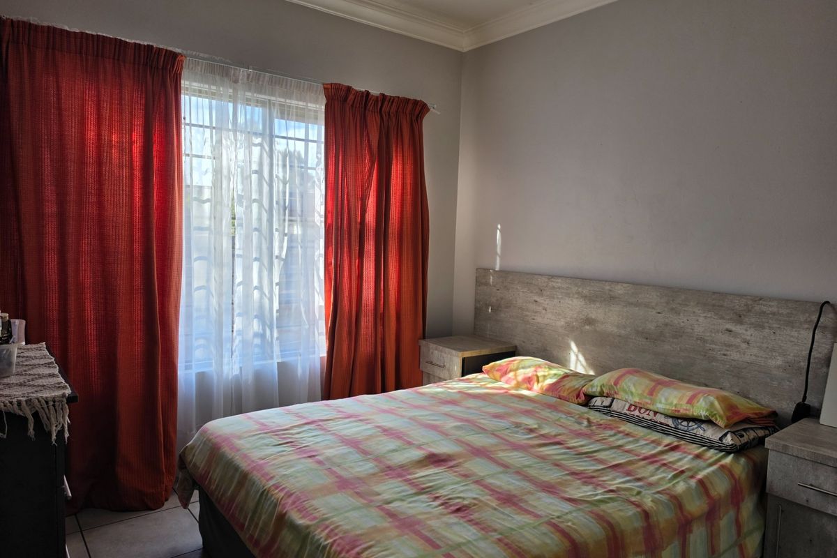 A bedroom featuring a built-in headboard and matching bedside pedestals, with tiled flooring and large windows dressed with curtains.