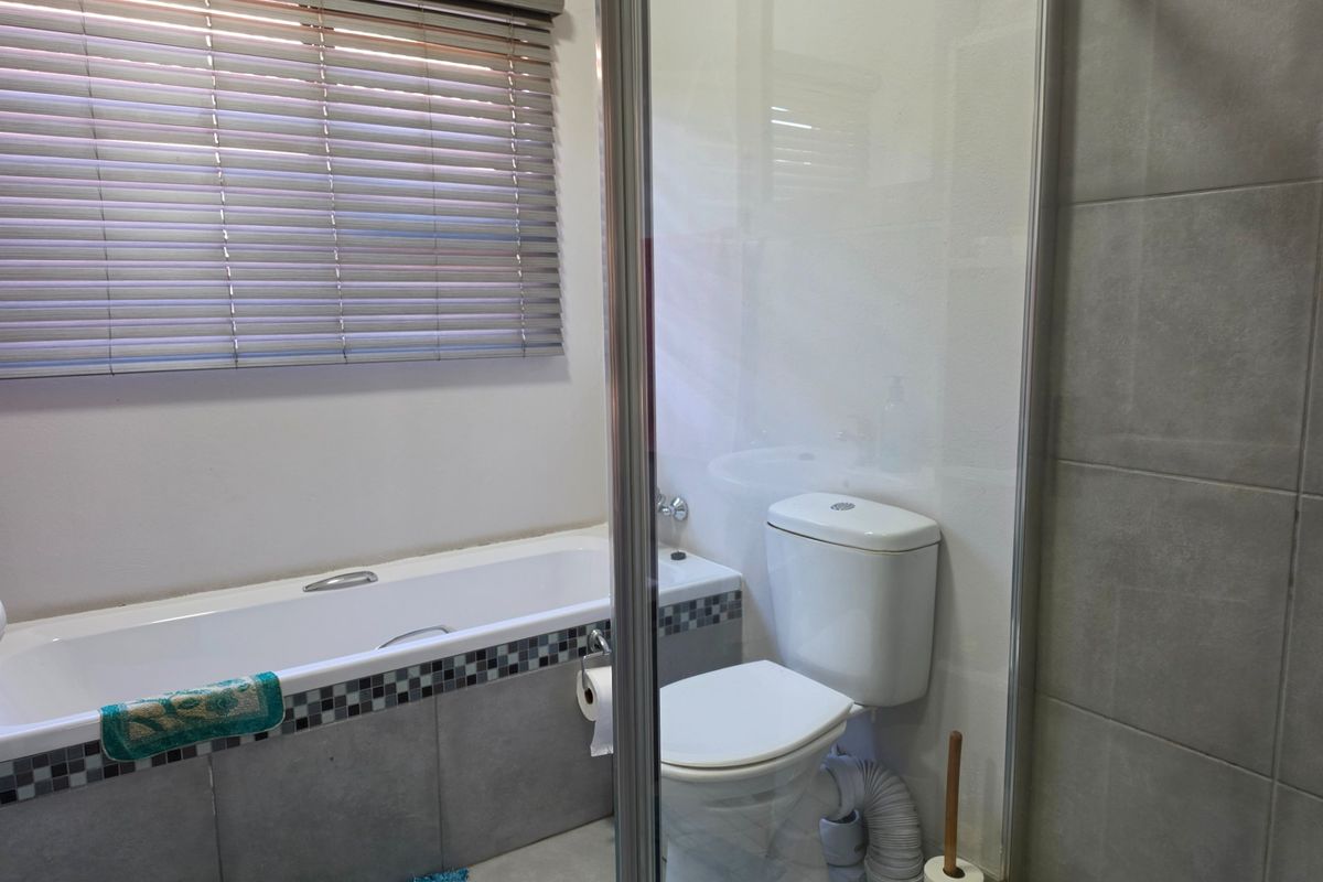 A functional bathroom featuring a bathtub with mosaic tile detailing, a toilet, and a glass-enclosed shower area with grey wall tiling.