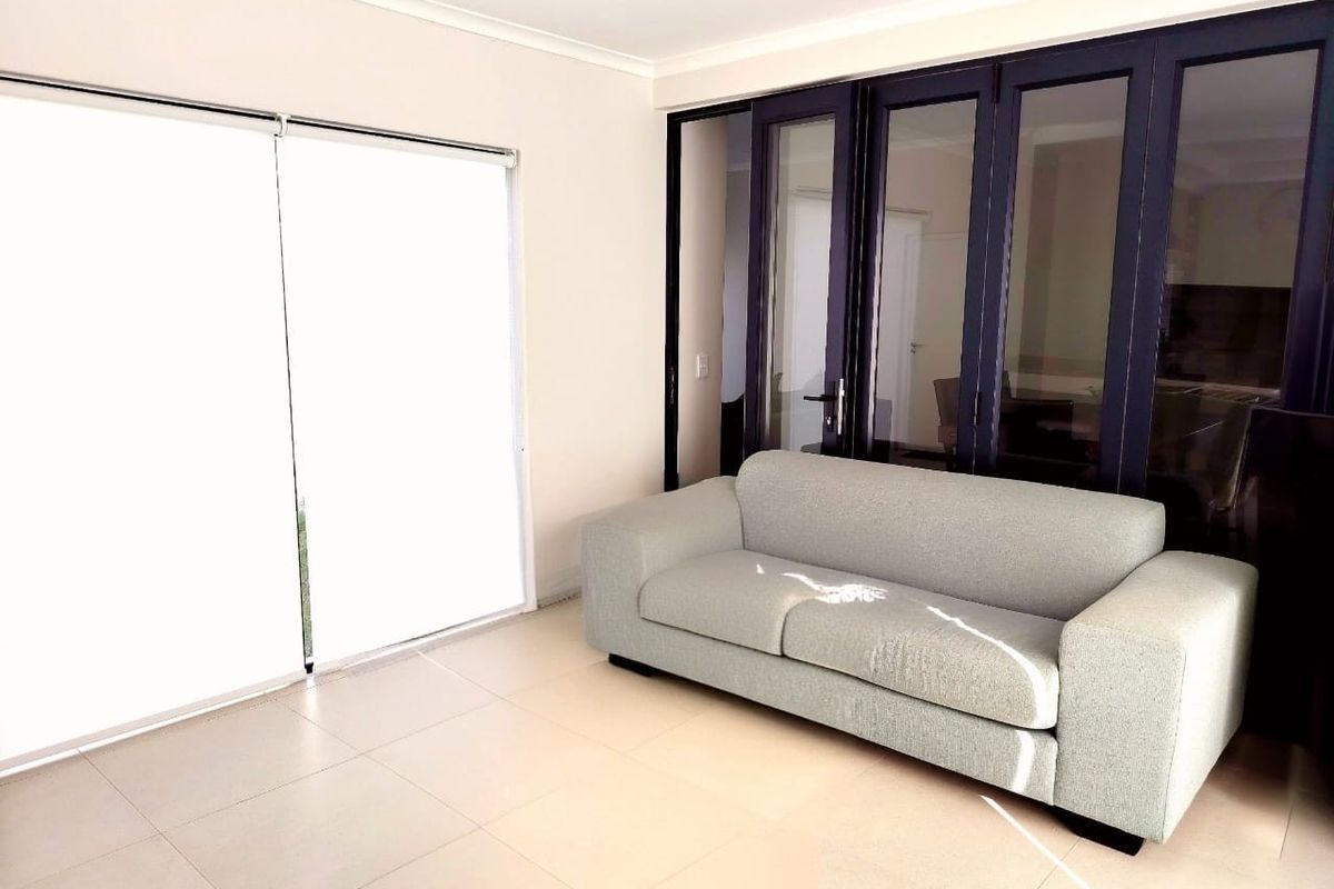 A bright living area featuring large tiled flooring, modern dark-framed glass sliding doors, and neutral wall finishes.