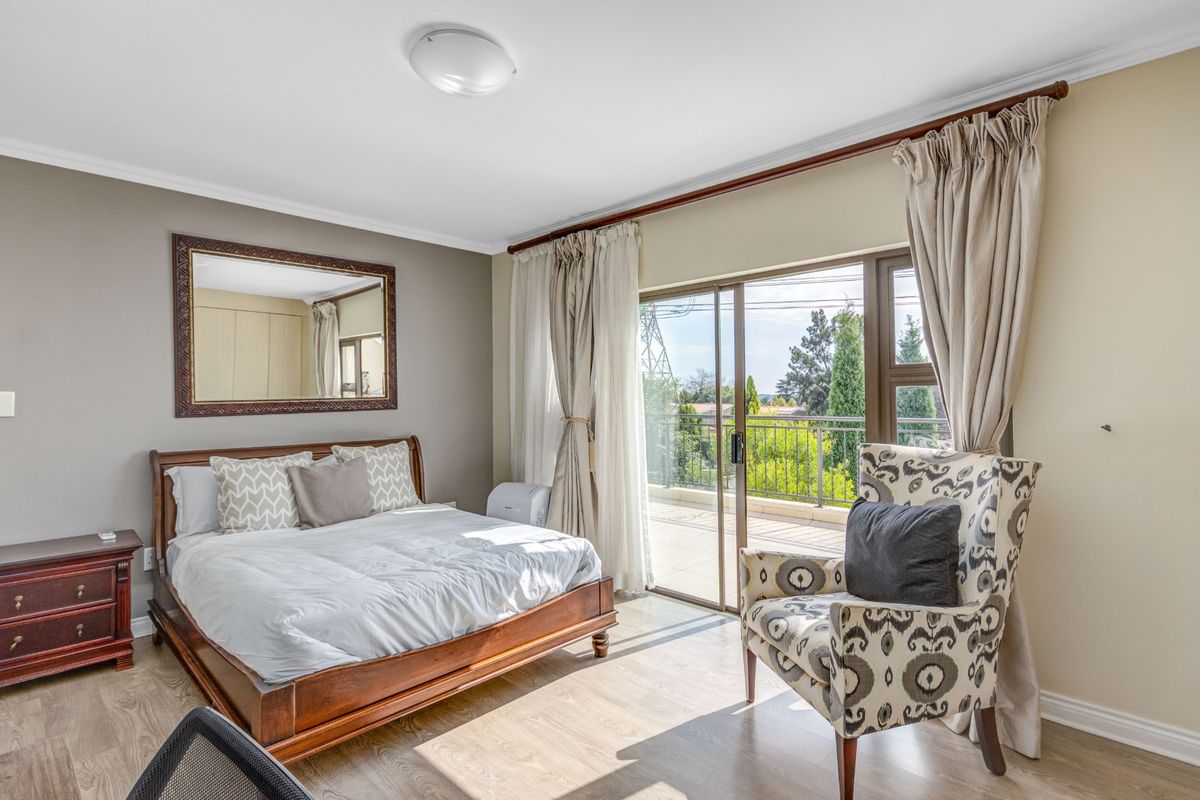 A well-lit bedroom featuring laminate flooring, built-in cupboards, and sliding glass doors that open onto a private balcony with scenic views.