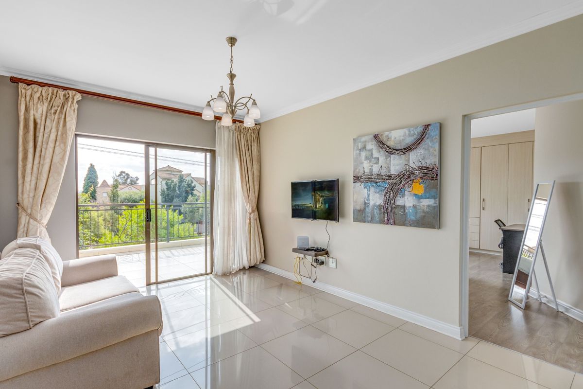 A bright living room featuring polished tile flooring, a decorative chandelier, and sliding glass doors that open onto a balcony with scenic views.