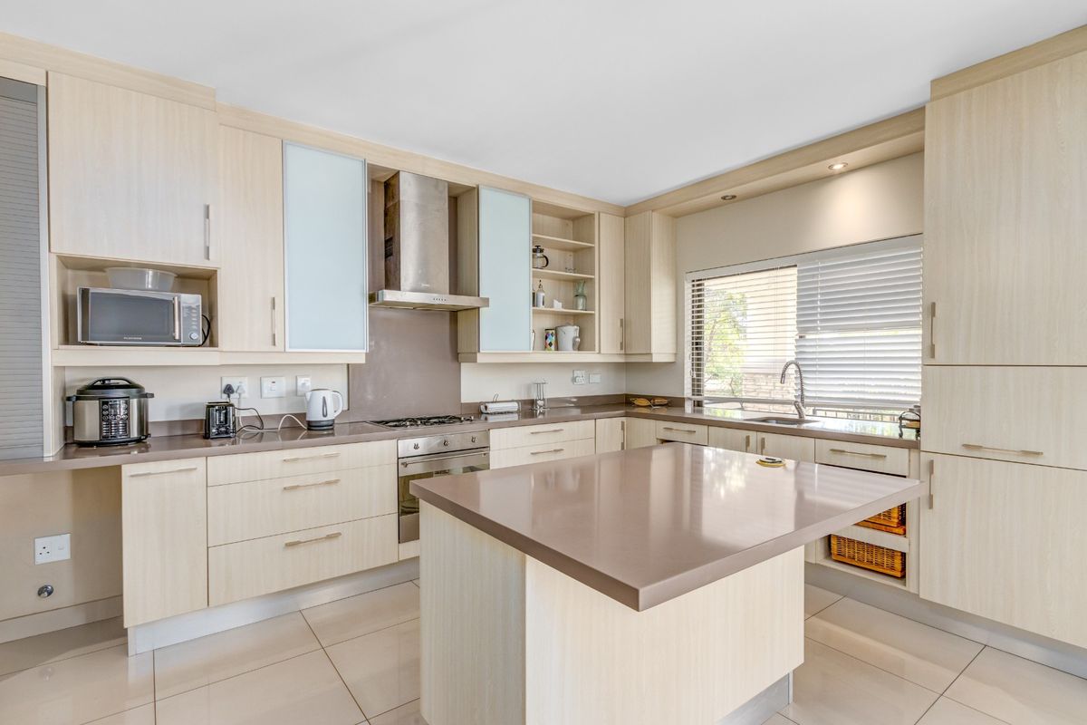 Modern kitchen featuring light wood cabinetry, stone countertops, a central island, stainless steel oven, gas hob, and a built-in extractor fan.