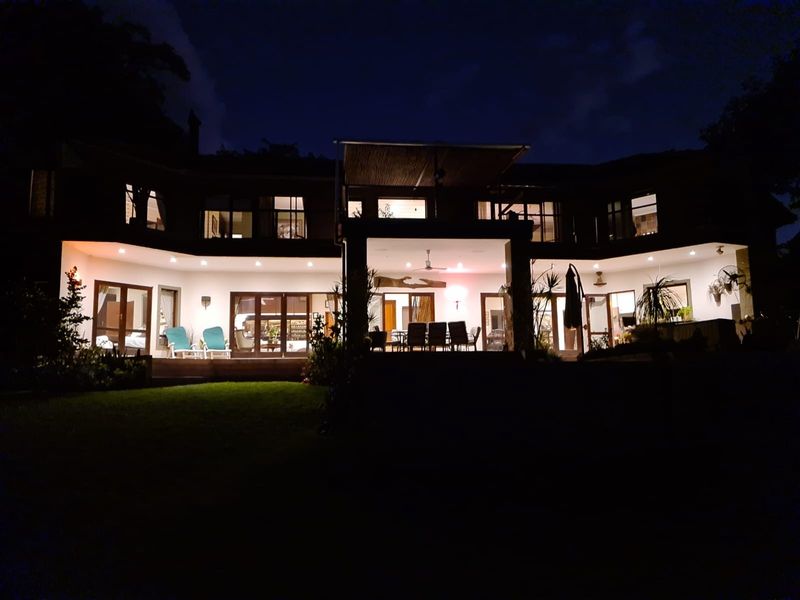 Night view of the rear elevation featuring a spacious covered patio, extensive glass sliding doors, and integrated outdoor lighting.
