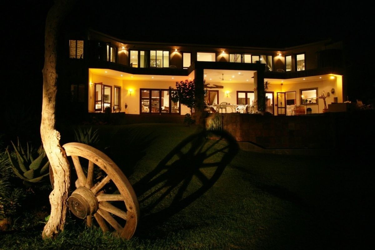 Night view of the rear elevation featuring a spacious covered patio, extensive glass sliding doors, and warm exterior accent lighting.