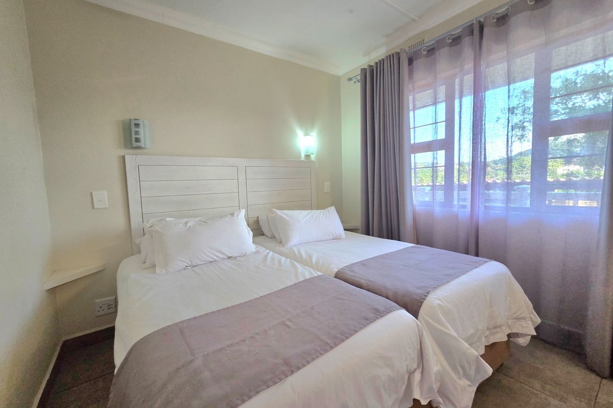 A well-maintained bedroom featuring tiled flooring, built-in wall lighting, and large windows with curtains, providing a comfortable and functional living space.