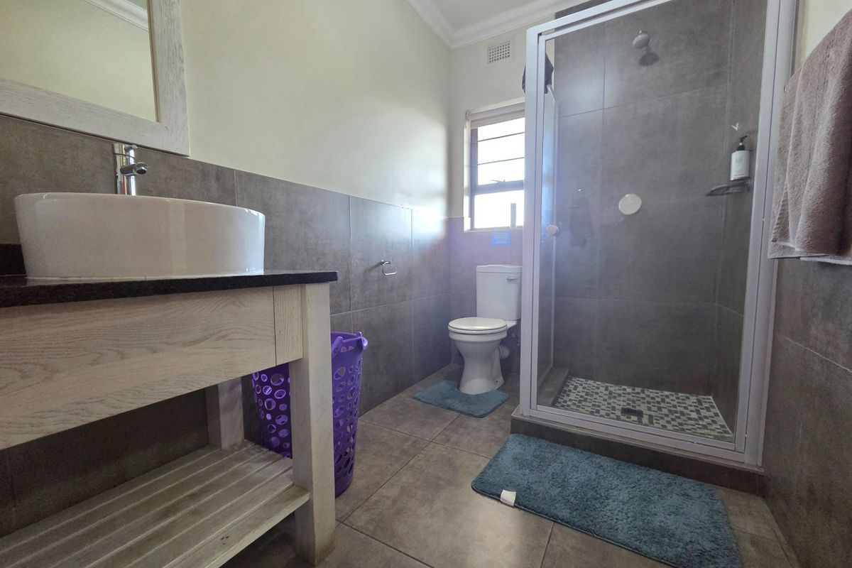 Modern bathroom featuring a vessel sink vanity, walk-in shower with glass enclosure, and neutral floor-to-ceiling tiling.