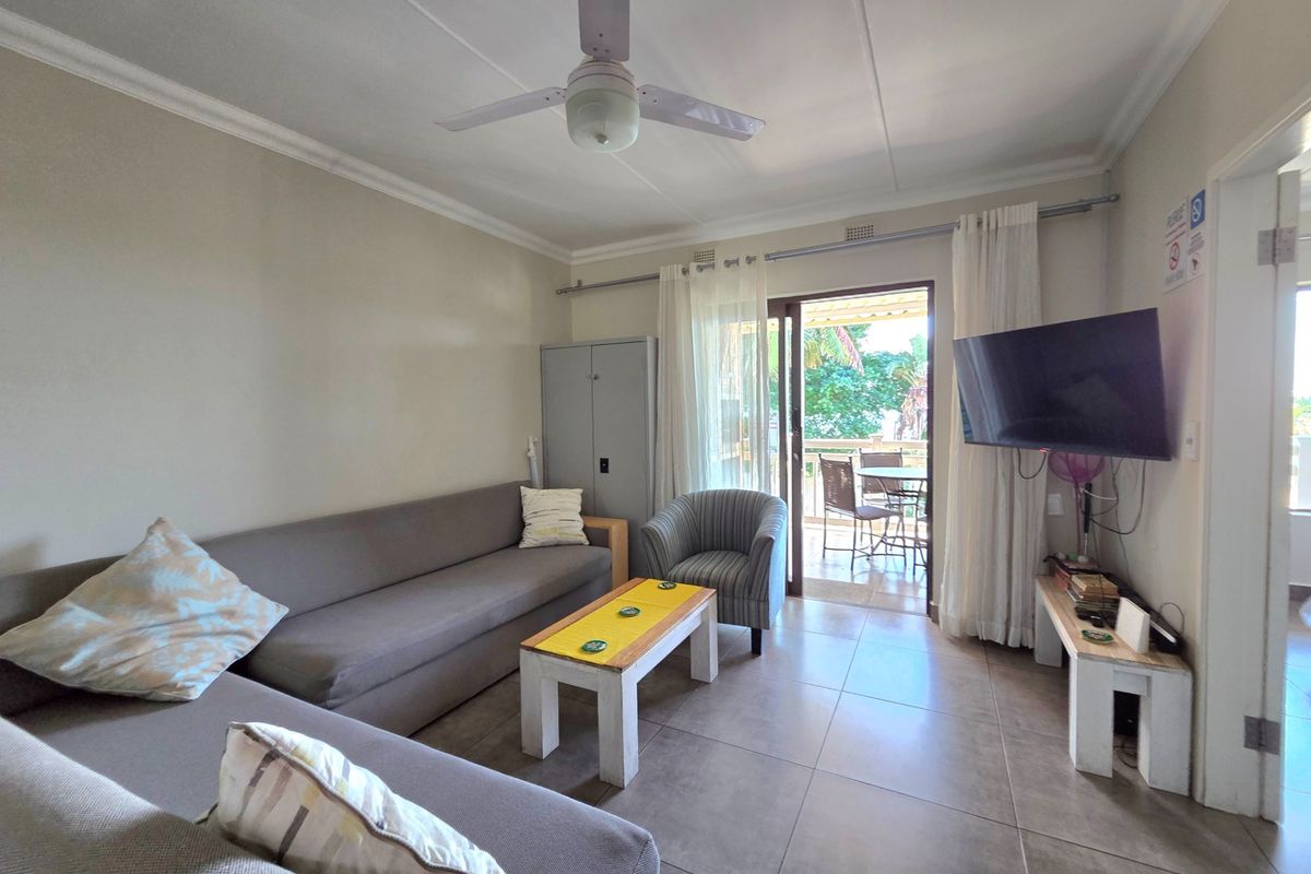 A comfortable living room featuring tiled flooring, a ceiling fan, and sliding glass doors that open onto a private balcony.