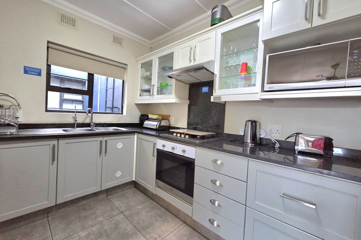 A well-maintained kitchen featuring light-toned cabinetry, dark granite countertops, a built-in oven, hob, extractor fan, and a double-basin sink.