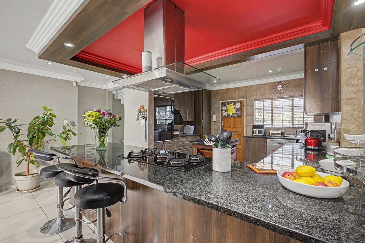 Modern kitchen featuring a large granite breakfast bar, built-in gas hob, stainless steel extractor fan, and dark wood cabinetry with a striking red ceiling feature.
