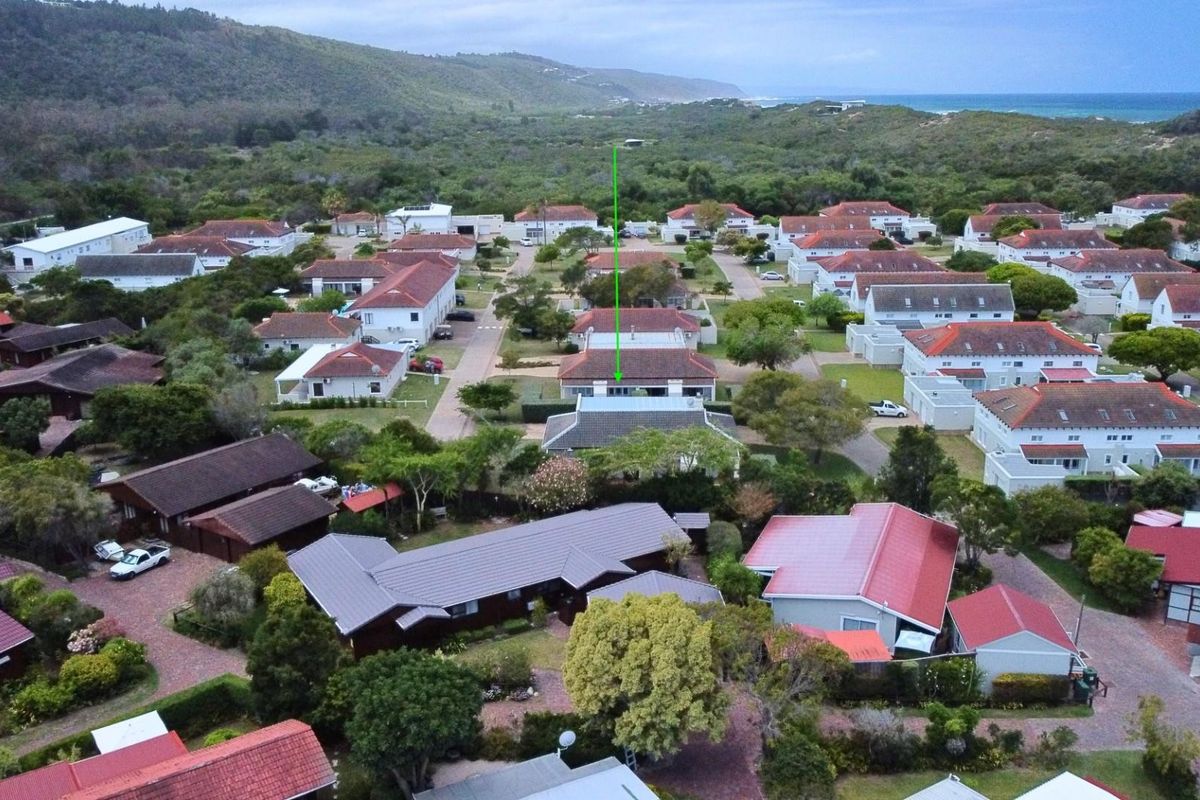 Aerial view of a residential estate featuring multiple detached houses with pitched roofs, surrounded by lush greenery and coastal landscape.